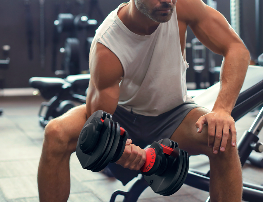 A bodybuilder using the SmartBell to do sitting bicep curls at his desired weight thanks to the adjustable dumbbell’s quick-select weight dial.